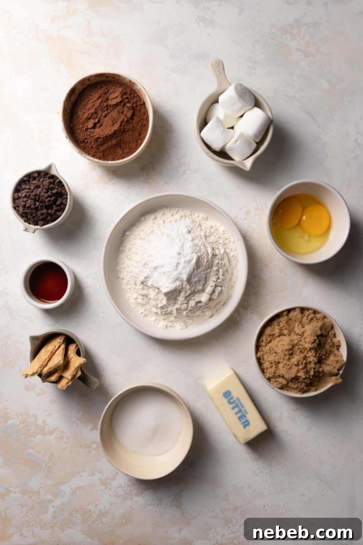 Bowls of ingredients arranged for making s'mores cookies, including chocolate chips, cocoa powder, marshmallows, and graham crackers.