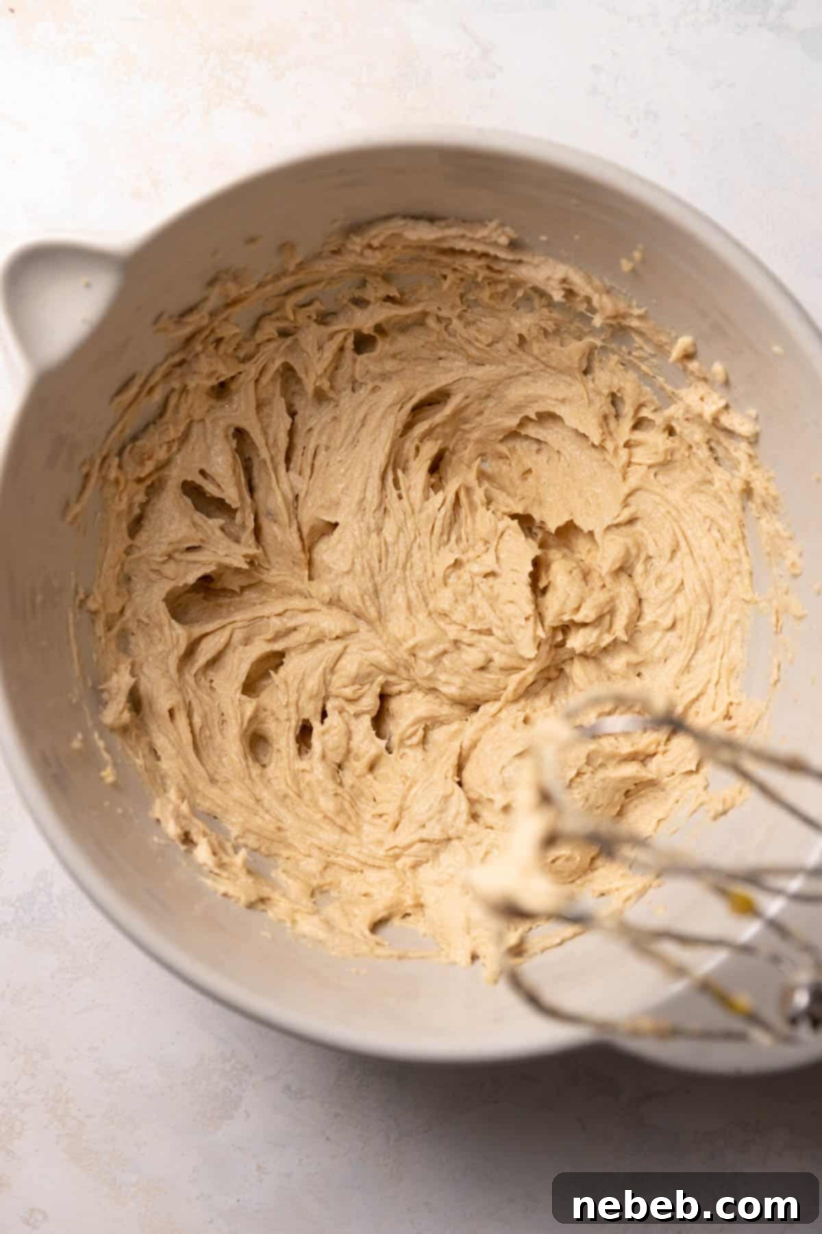A mixing bowl showing wet cookie dough after eggs and vanilla have been incorporated.