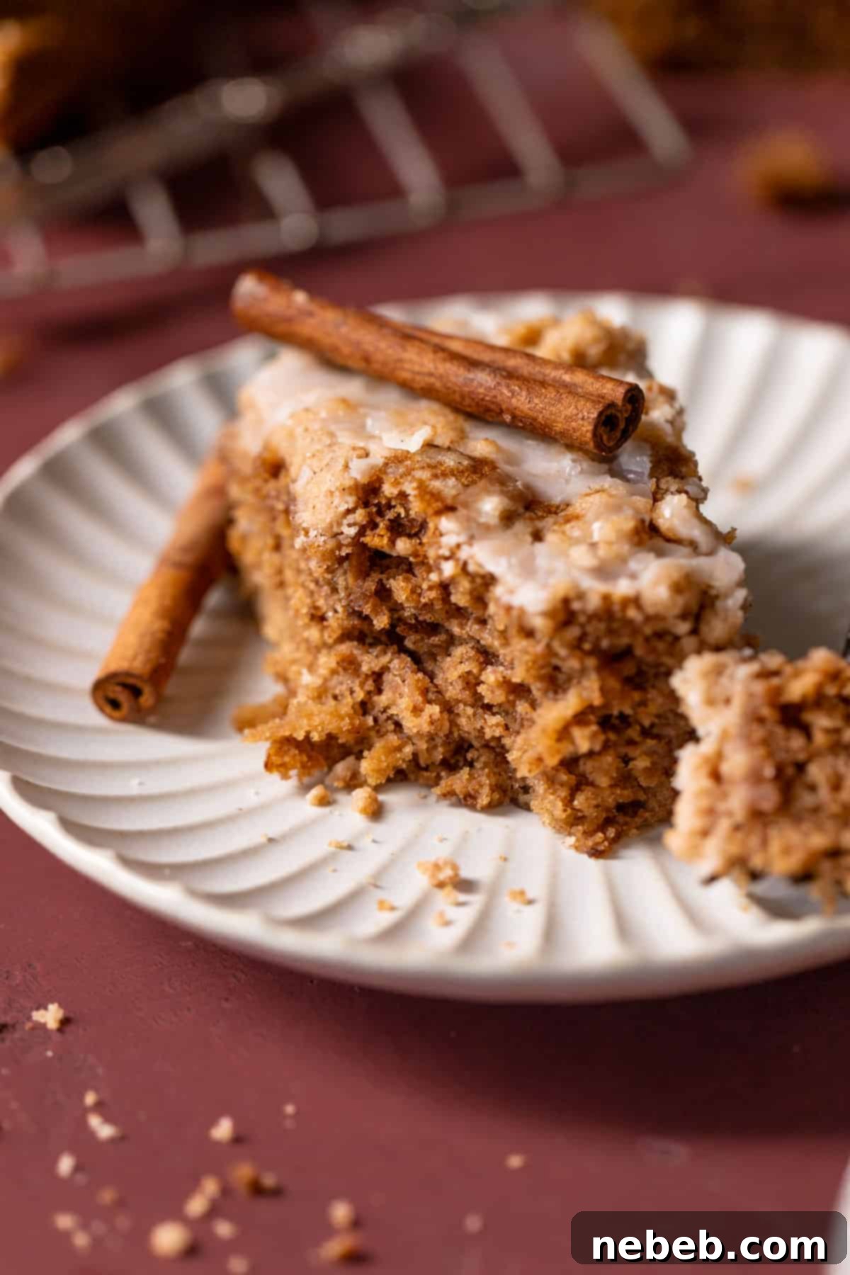 Best Ever Cinnamon Apple Cake 10 A perfectly sliced piece of cinnamon apple cake on a white plate, garnished with a cinnamon stick, showcasing its beautiful crumb and inviting glaze.