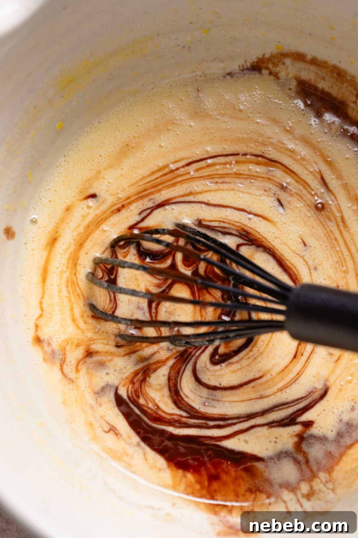 A whisk mixing the melted chocolate mixture into the eggs and sugar.