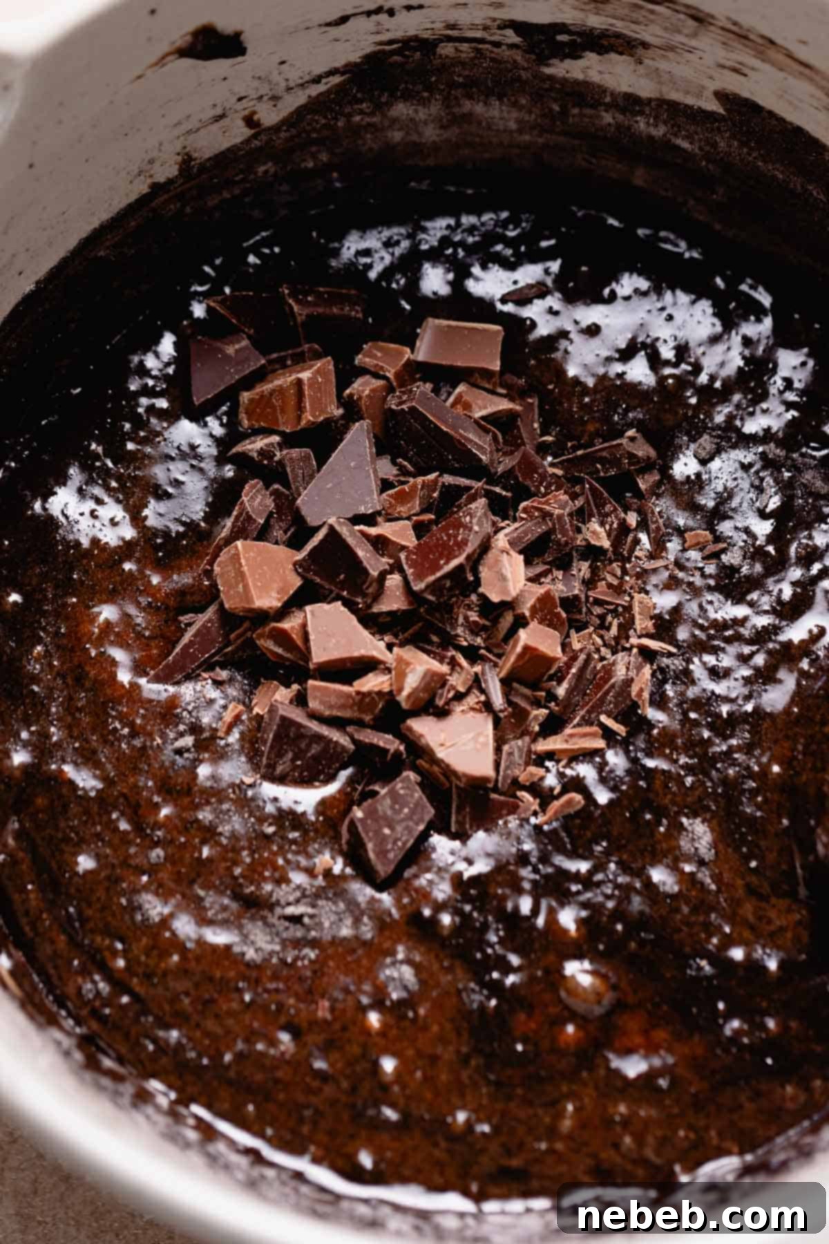 A mixing bowl of brownie batter with chocolate pieces on top before mixing.