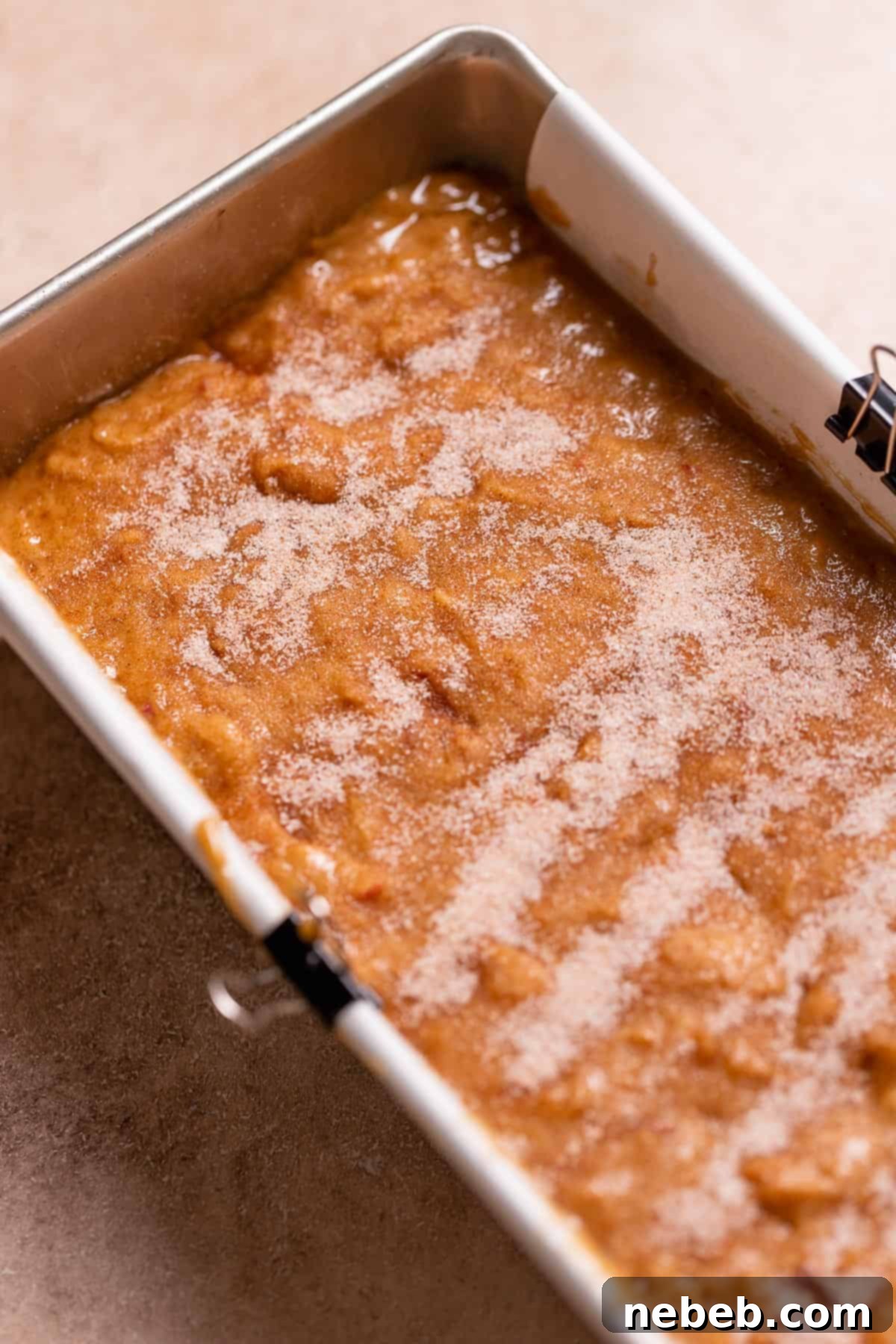 A loaf pan full of apple donut batter sprinkled with cinnamon sugar.