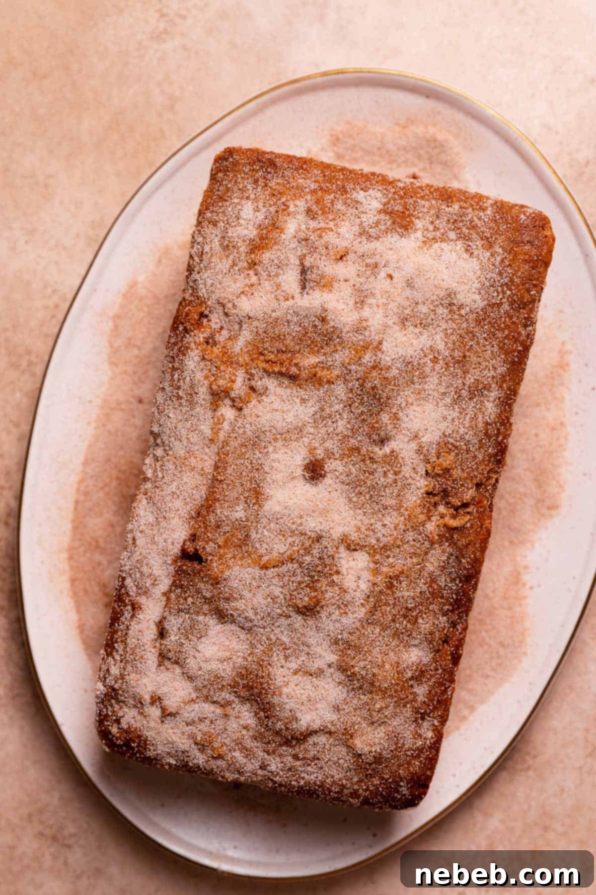 The cinnamon donut cake on a white plate being coated in cinnamon sugar.