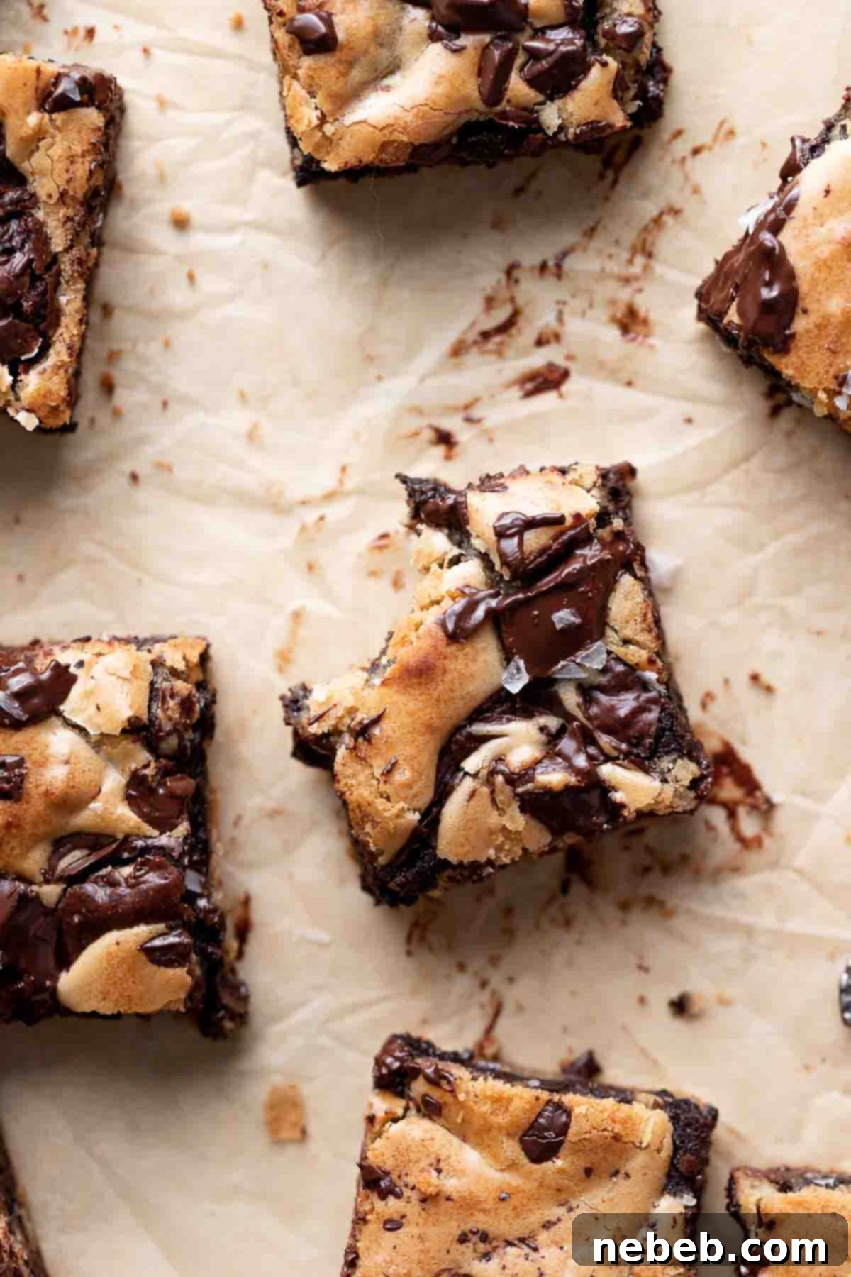 Brownie Blondie Bliss 7 A close-up of several perfectly cut brownie blondies resting on parchment paper, with a delicate sprinkle of flaky sea salt on top to enhance their rich flavors.