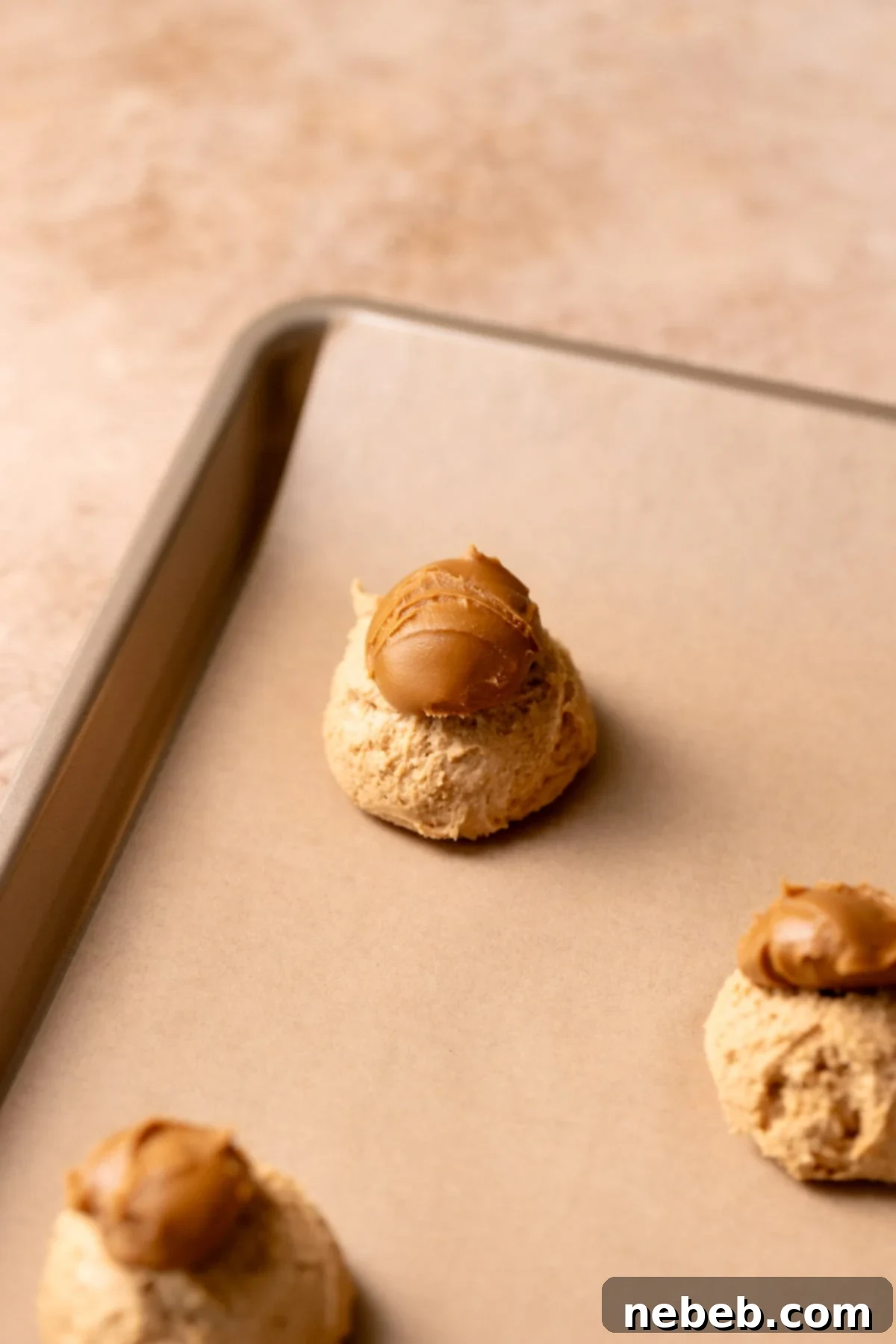 A cookie dough ball on a baking sheet with a glob of Biscoff cookie butter on top.