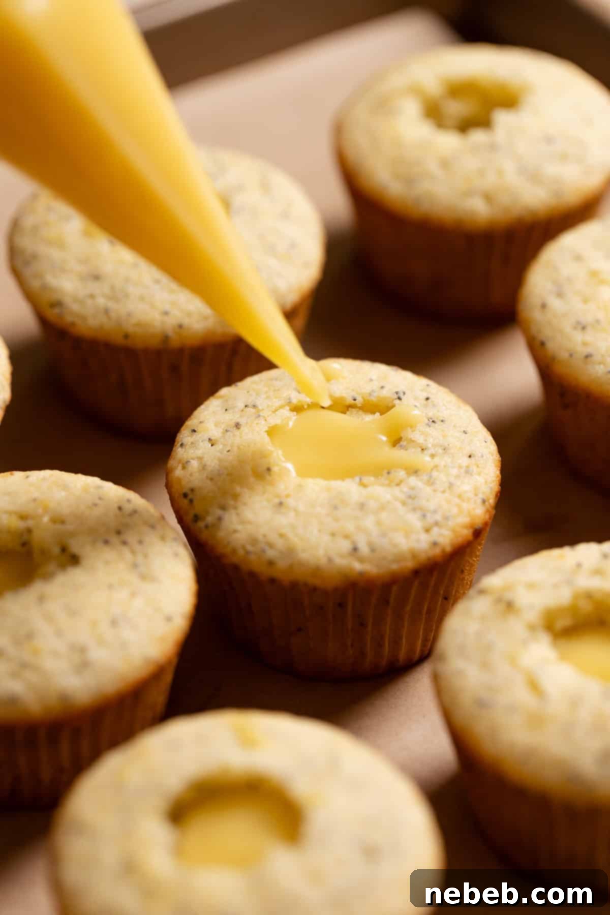A piping bag precisely filling a cored lemon cupcake with sweet and tangy lemon curd.