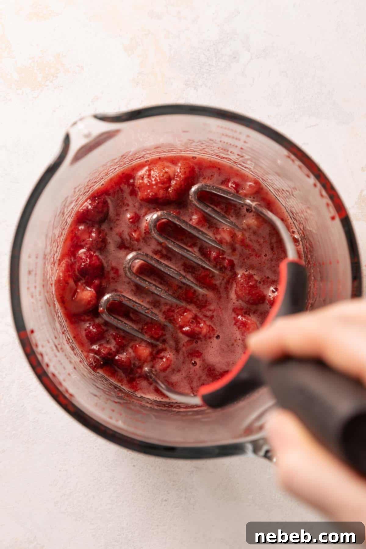 Golden Crunch Strawberry Cupcakes 3 Mashing roasted strawberries in a glass mixing bowl for strawberry crunch cupcakes, highlighting the rich, concentrated fruit flavor.