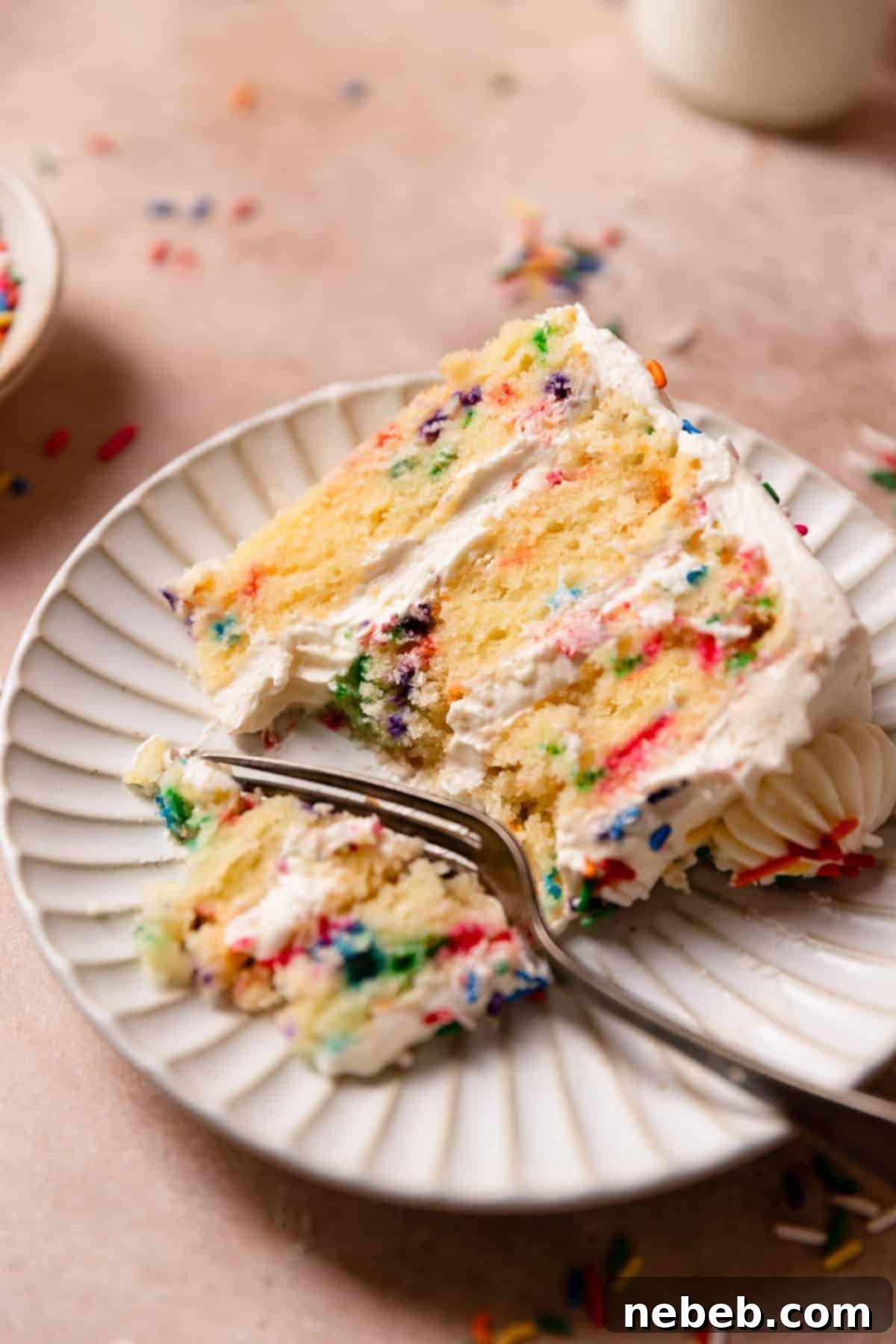 A beautifully sliced funfetti cake on a white plate, with a fork poised to take a bite, showcasing the vibrant sprinkles within the moist cake layers and smooth vanilla buttercream.