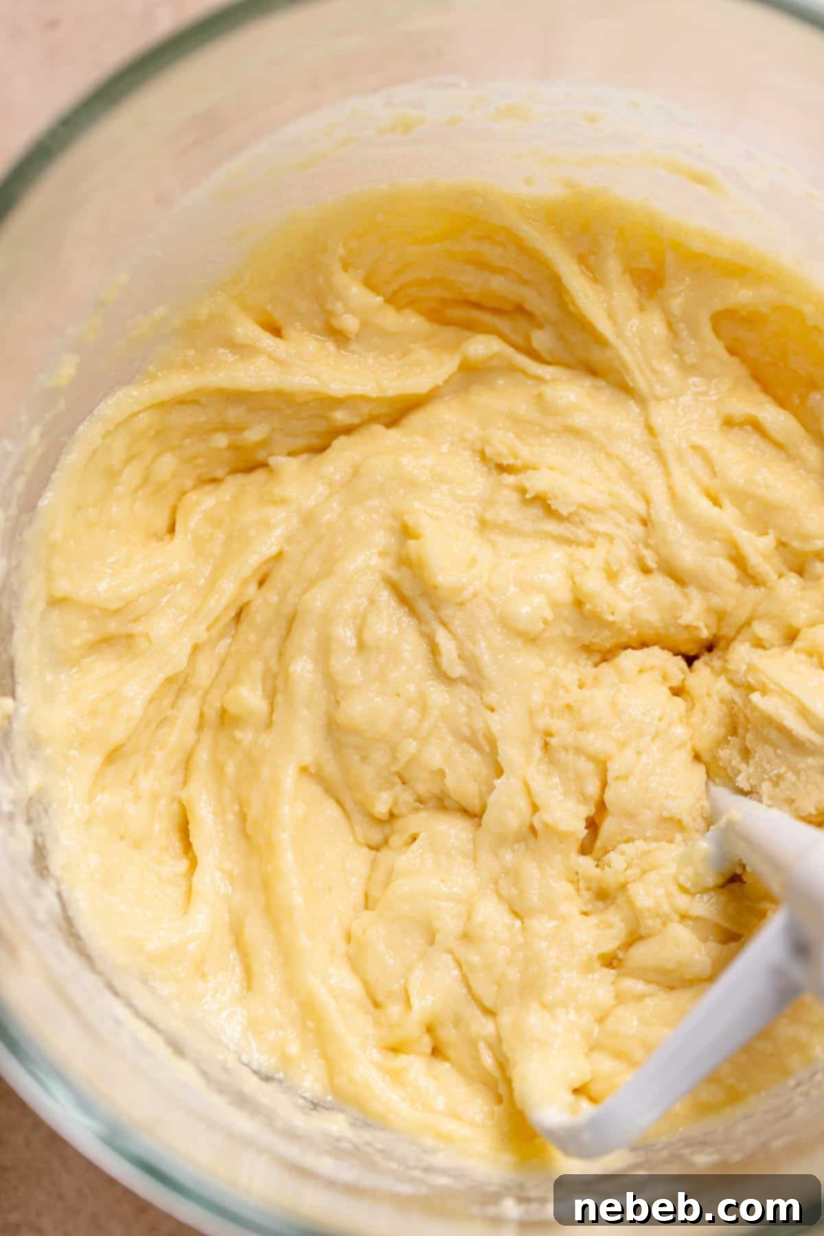 White cake batter in a stand mixer bowl, mixed to a thick, pasty consistency.