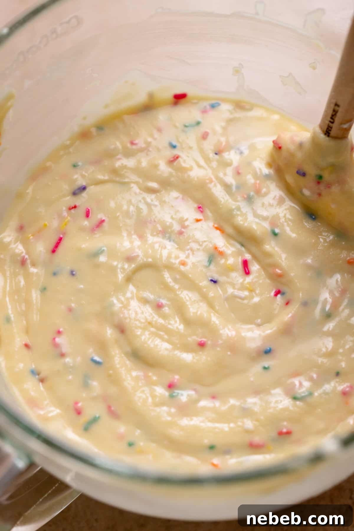 Vibrant funfetti sprinkle cake batter in a clear glass stand mixer bowl, ready for baking.