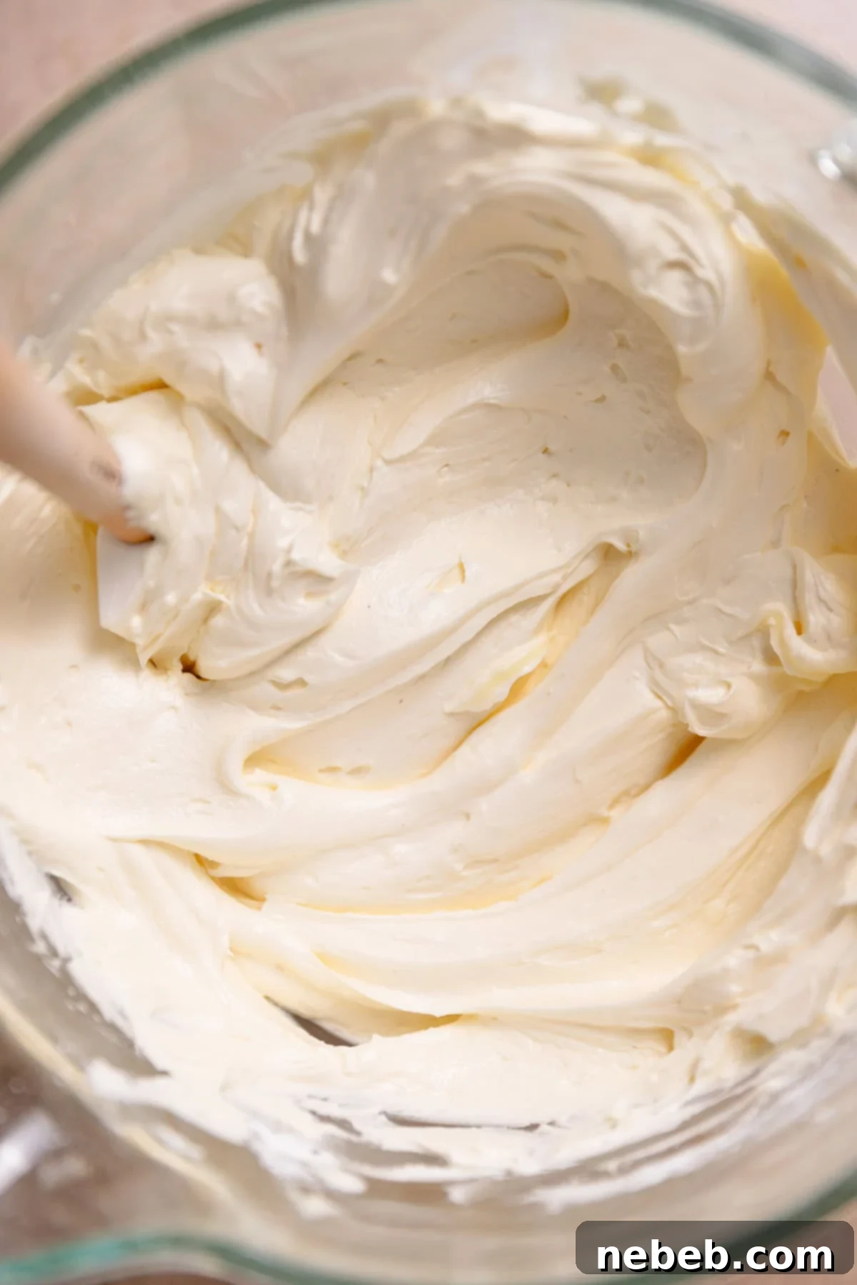 Smooth, creamy vanilla buttercream frosting in a glass mixer bowl, with a spatula resting inside.