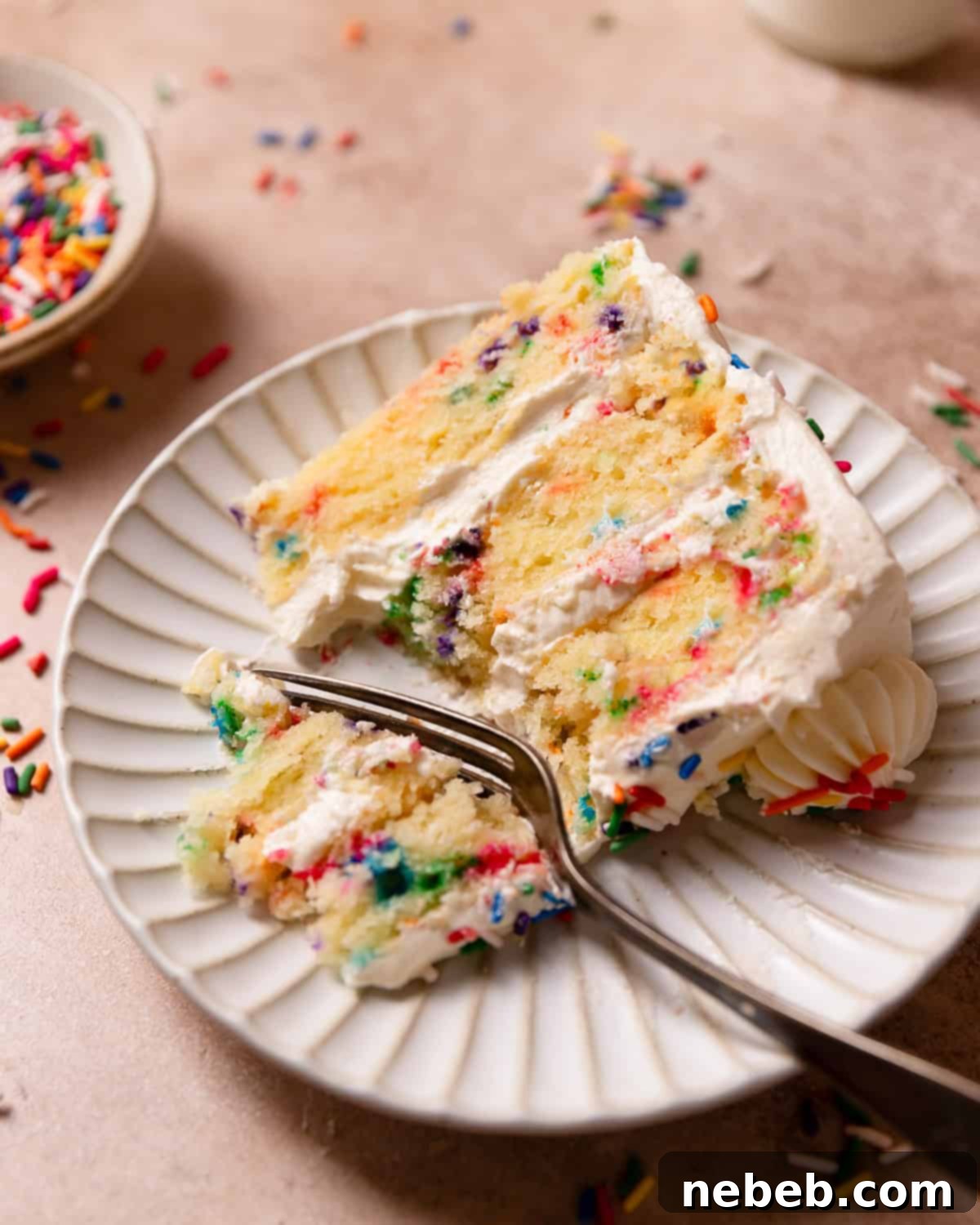 A perfectly portioned slice of funfetti cake on a white plate with a fork, highlighting the soft texture and abundant sprinkles.