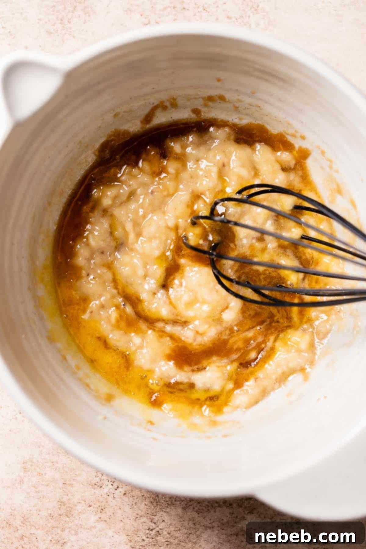 A bowl of whisked banana, butter, egg, and sugar.