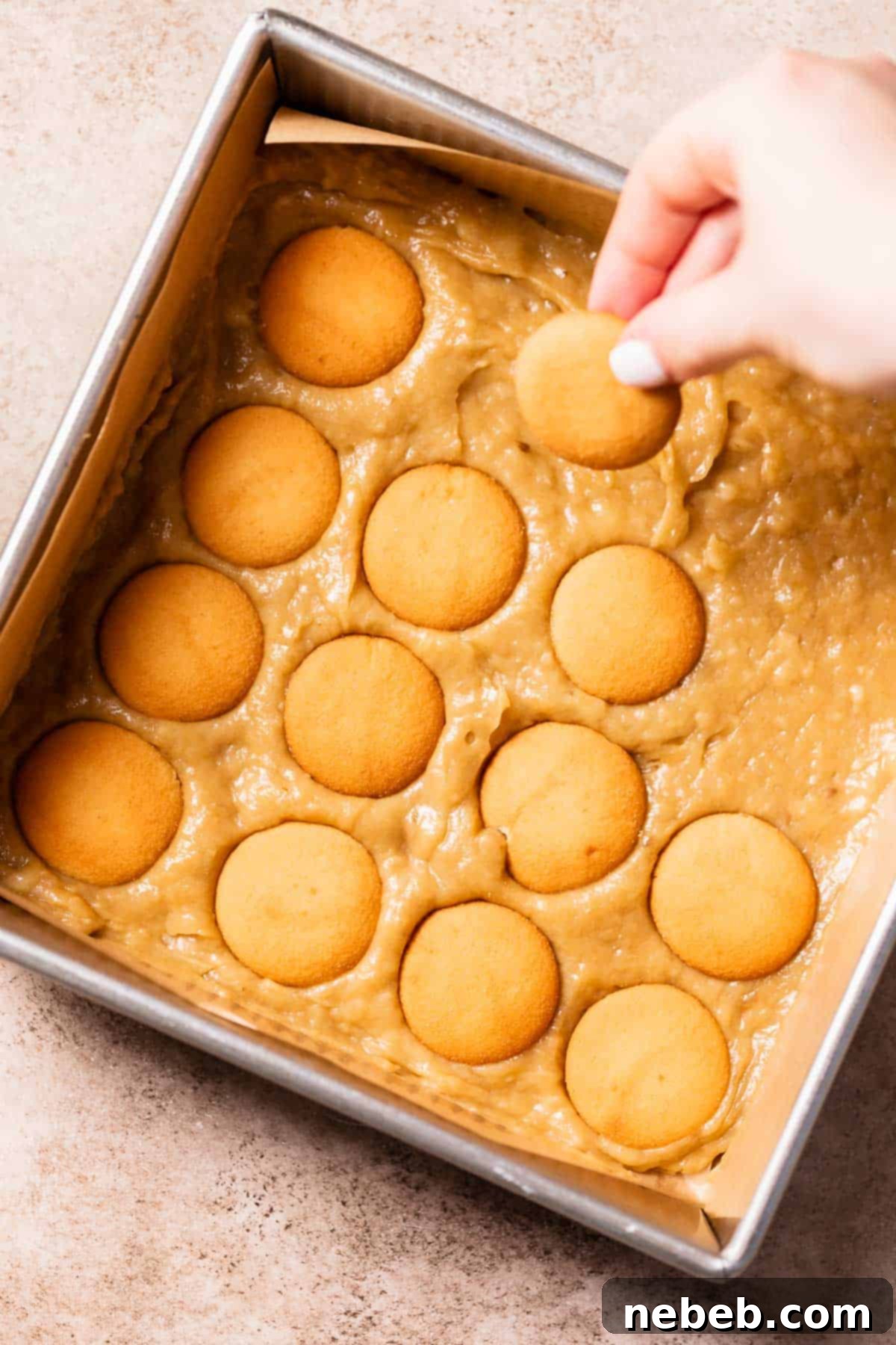 A hand pressing vanilla wafer cookies into the banana batter.