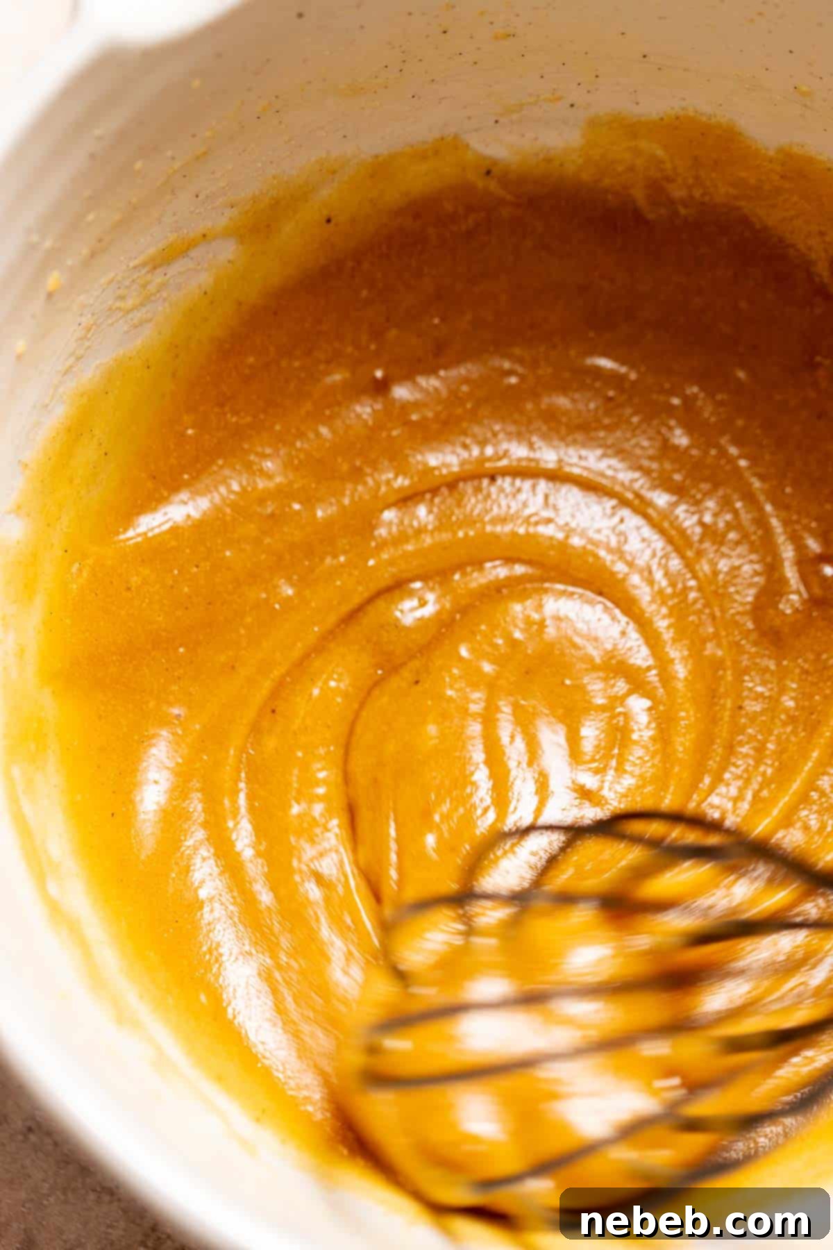A whisk mixing together the brown butter, sugars, and eggs.