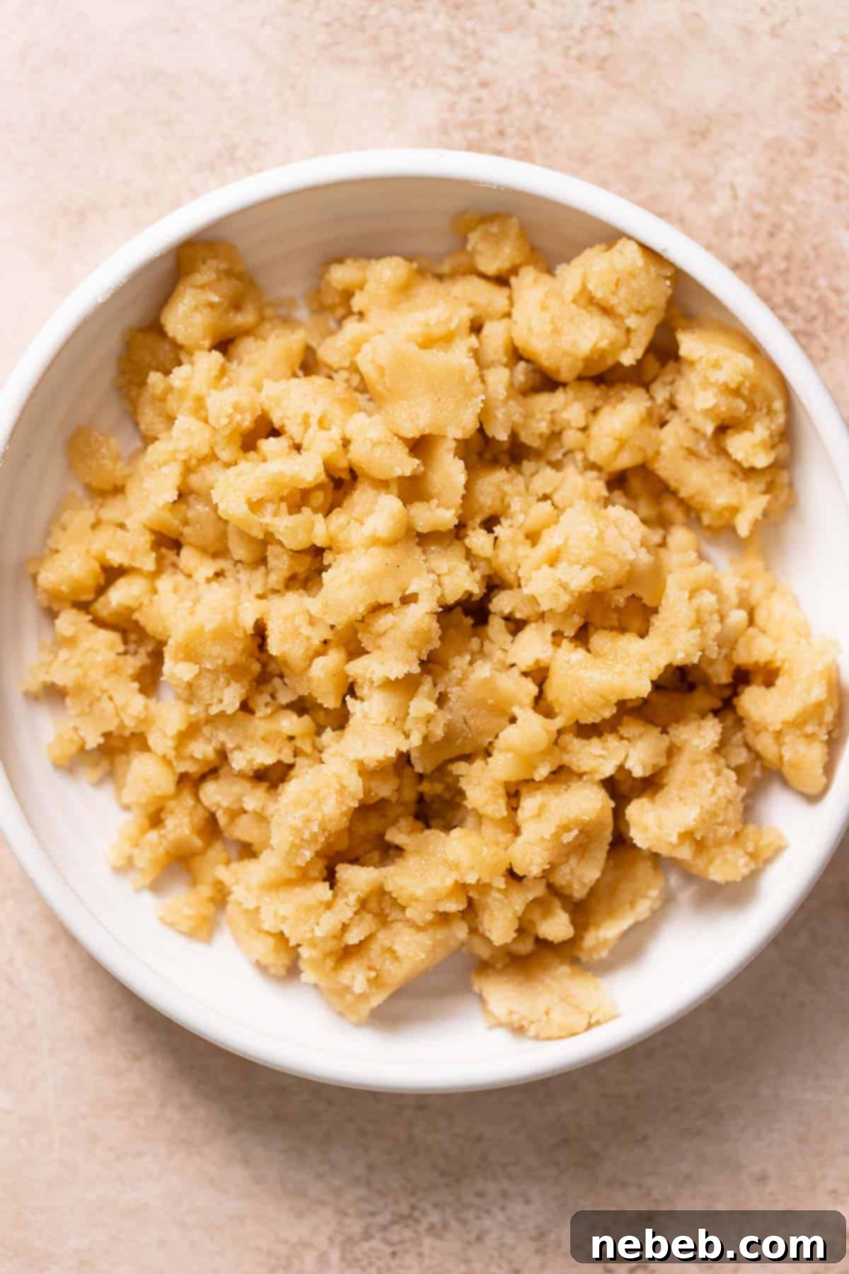 A white bowl filled with the buttery crumb topping mixture, ready to be sprinkled.