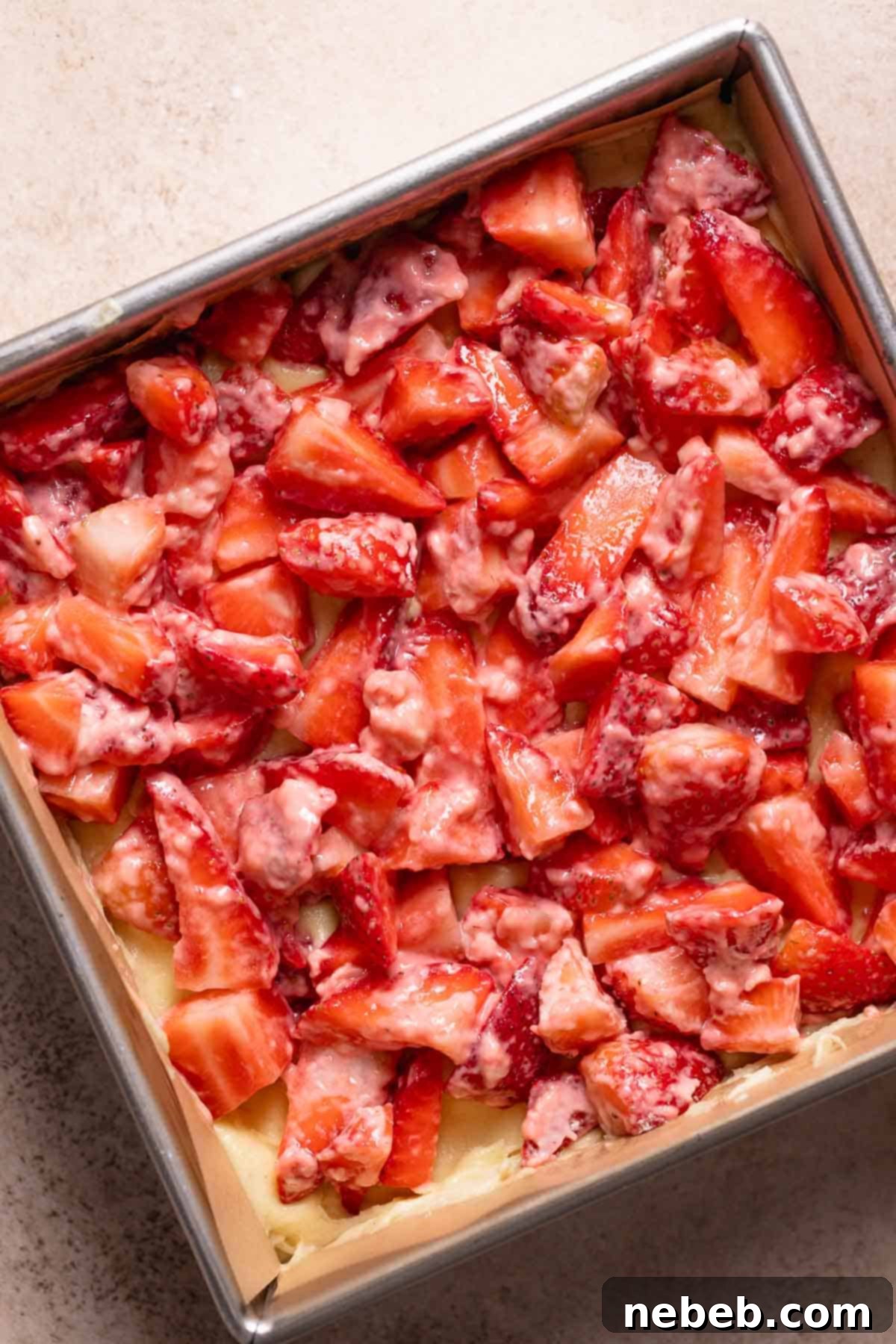 An overhead view of macerated strawberries being carefully spread over the vanilla cake batter.