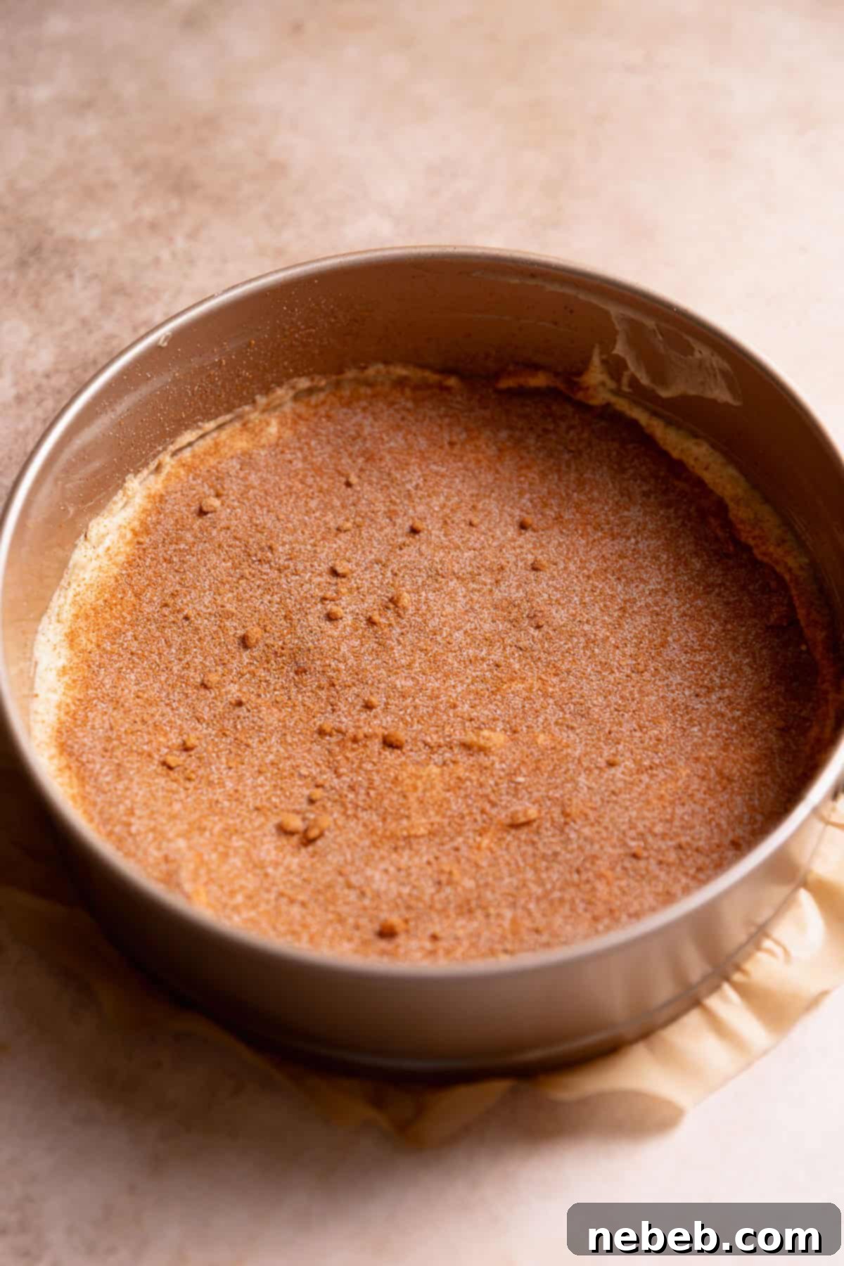 A layer of coffee cake batter in a round baking pan with cinnamon sugar sprinkled on top.