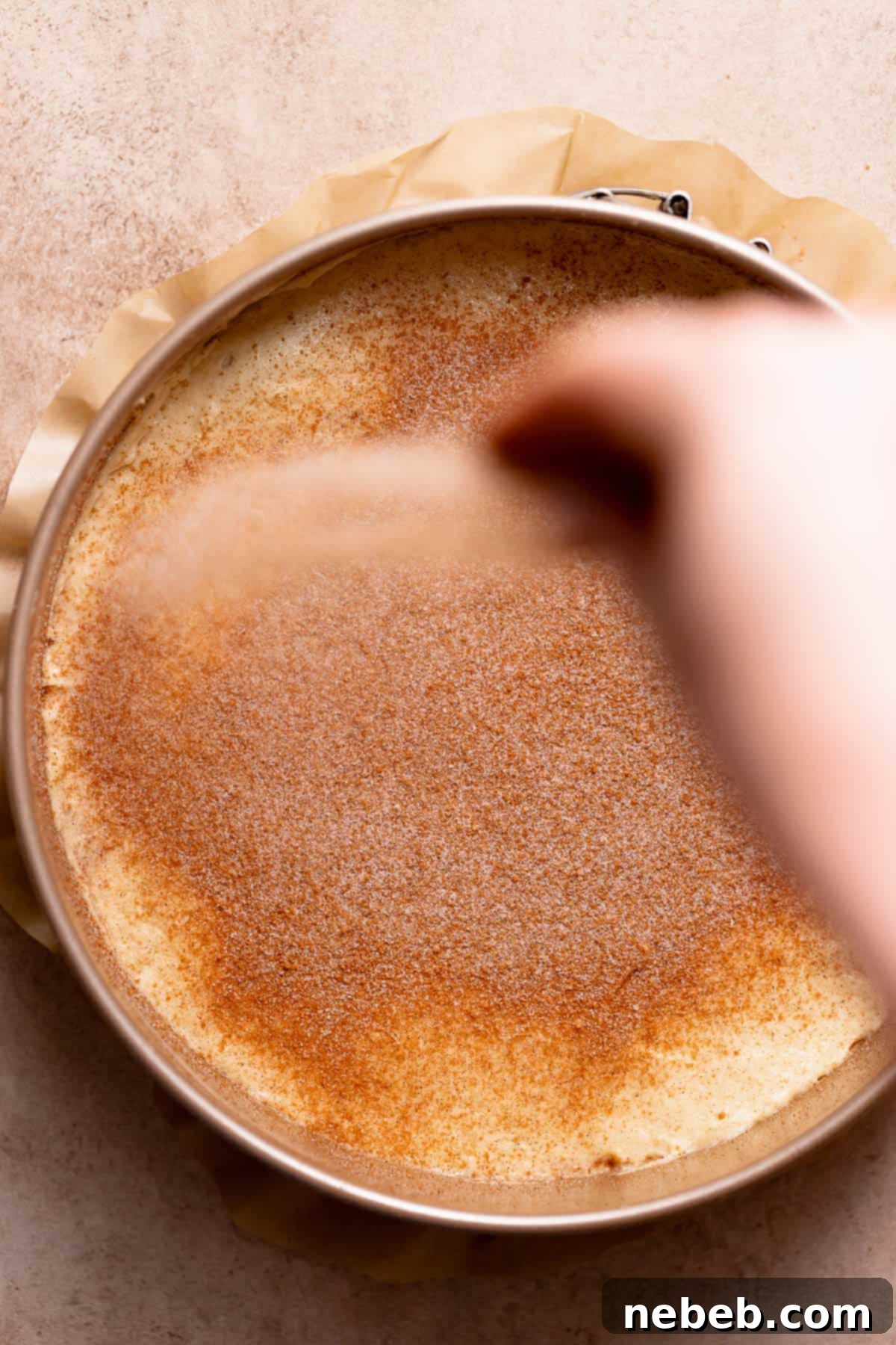 A hand covering the top of the cinnamon coffee cake with brown sugar cinnamon streusel.