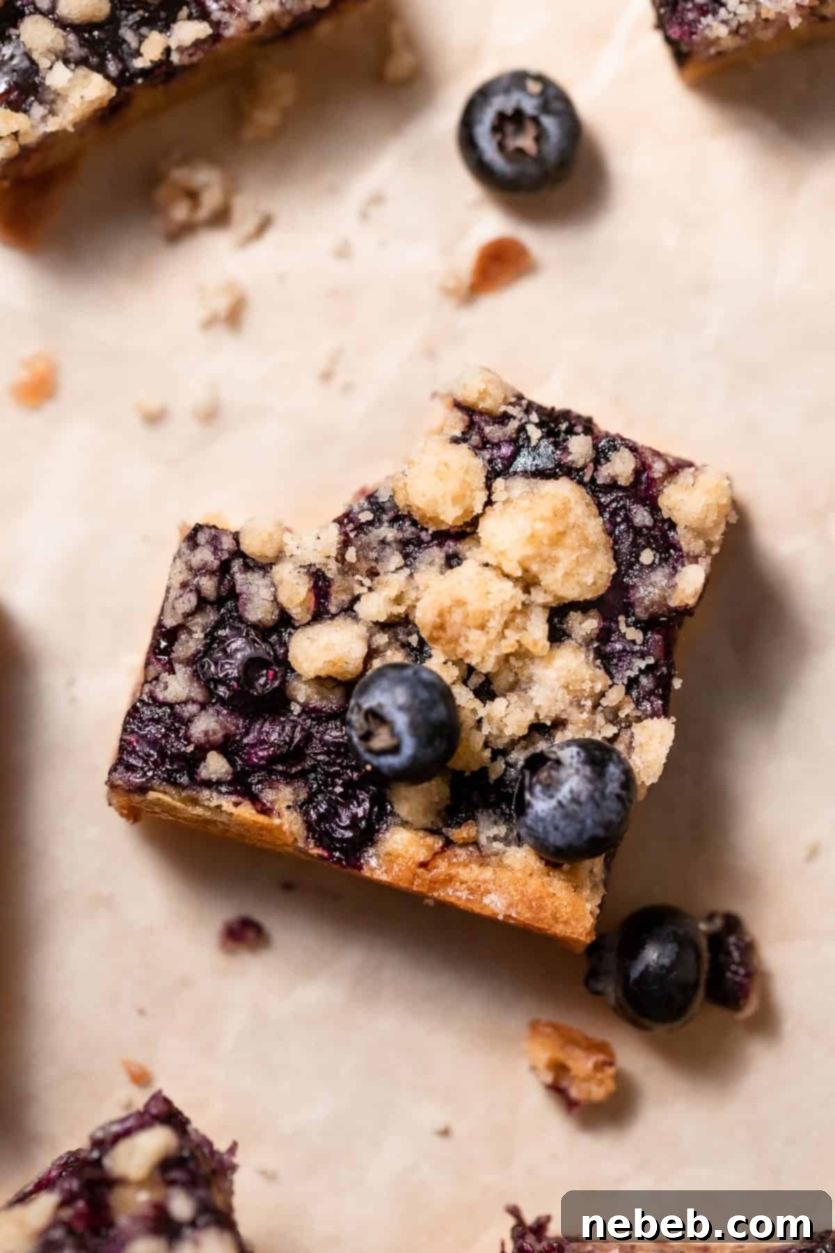 A delicious blueberry blondie with a bite taken out of it, showcasing the rich layers of chewy blondie, vibrant blueberry jam, and crisp crumb topping.