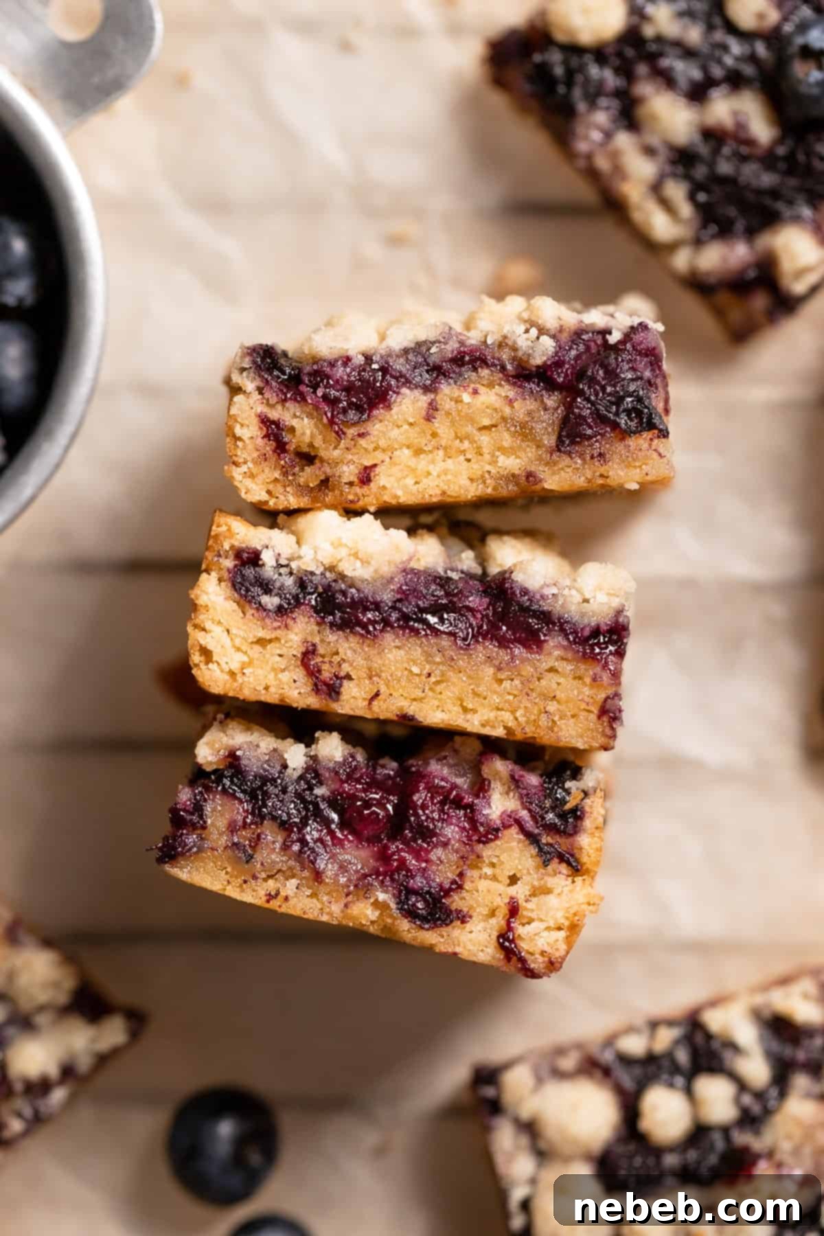 Freshly baked blueberry blondies layered with homemade jam and a golden crumb topping, cooling on parchment paper on a wire rack.