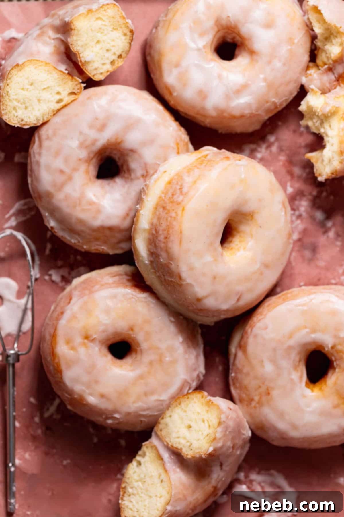 Pillowy Milk Bread Donuts 2 Glazed doughnuts on parchment paper with a few ripped in half to show the soft texture.