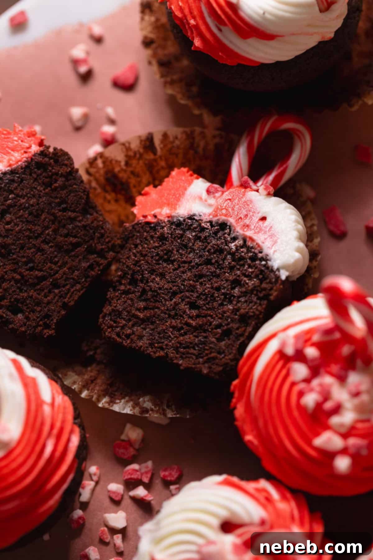 Chocolate peppermint cupcake with red and white swirled peppermint frosting cut in half on parchment paper. A perfect holiday treat.