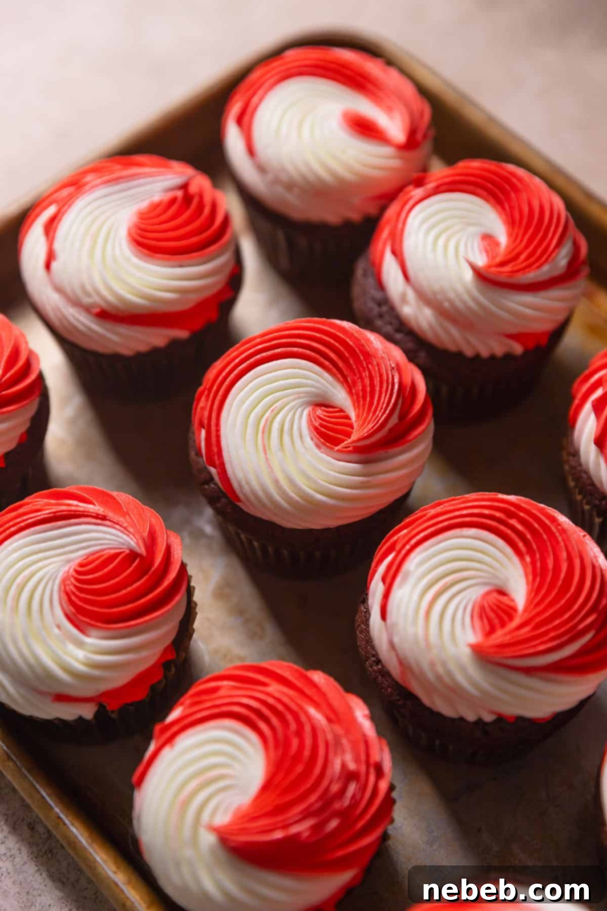 Freshly baked chocolate peppermint cupcakes adorned with beautiful red and white swirled peppermint frosting, topped with crushed candy canes and peppermint chips, displayed on a baking tray.