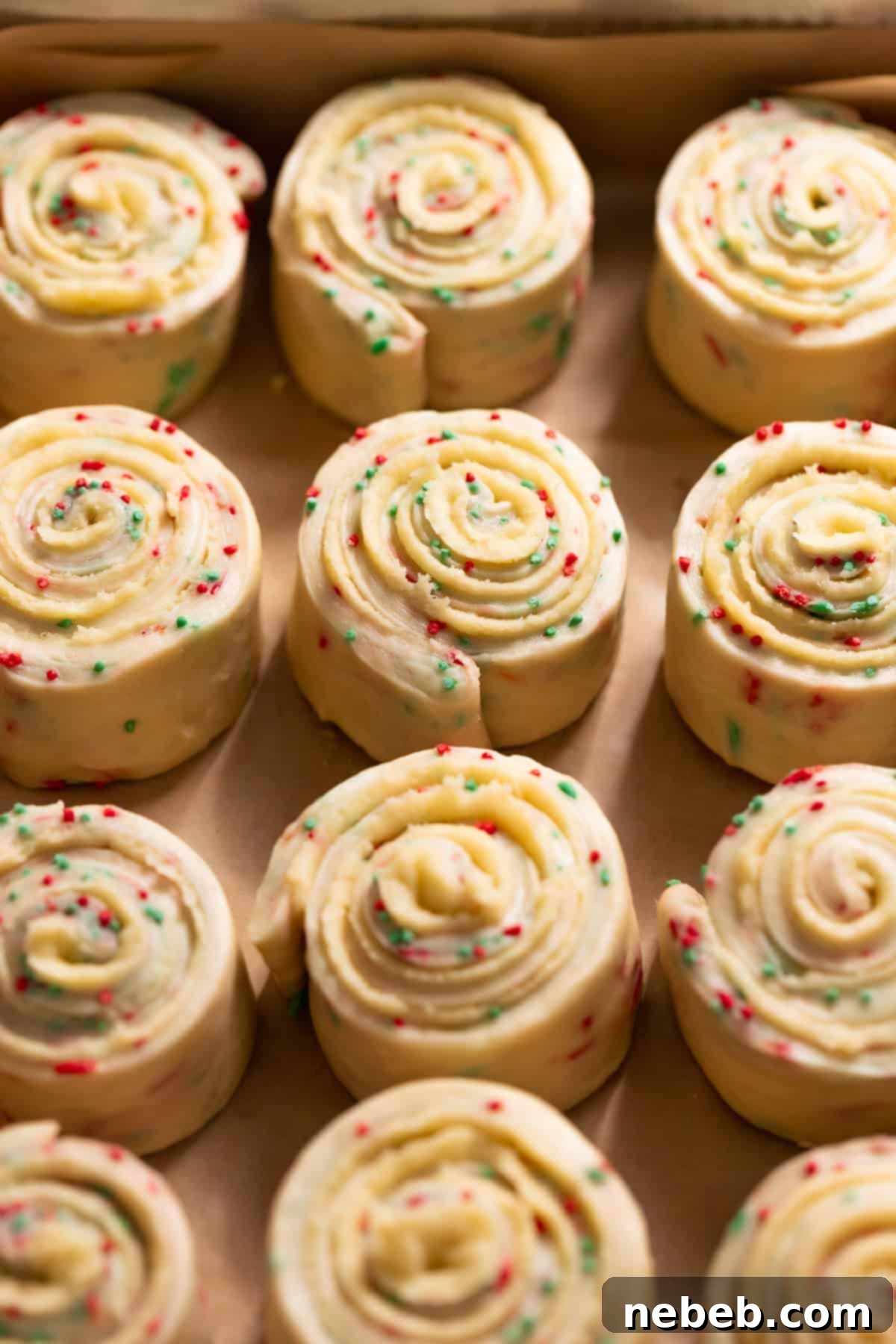 Christmas Swirl Sugar Cookie Bites 6 Unbaked sugar cookie rolls with beautifully tight spirals and holiday sprinkles, neatly arranged in a baking pan.