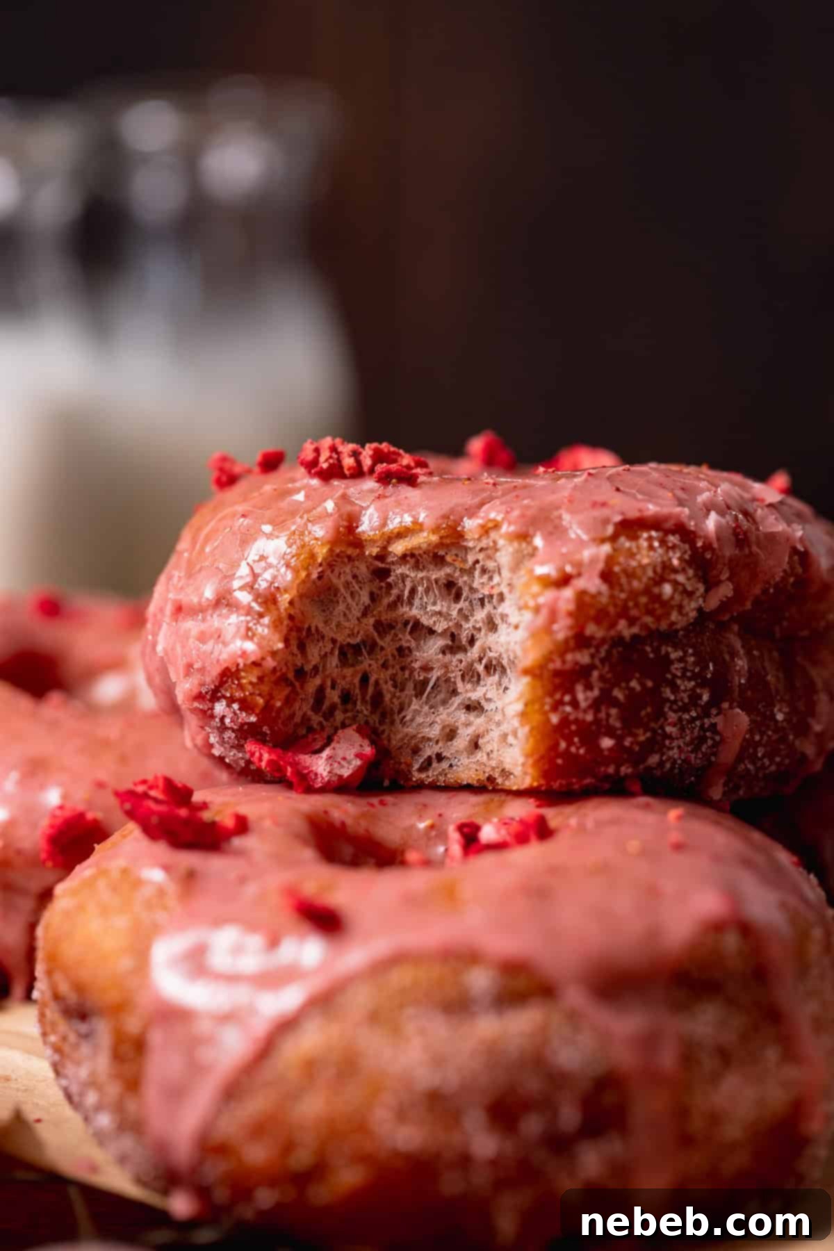 Triple Strawberry Dream Donuts 9 Strawberry-glazed donut with a bite taken out, showing the soft, fluffy interior and topped with crushed freeze-dried strawberries.